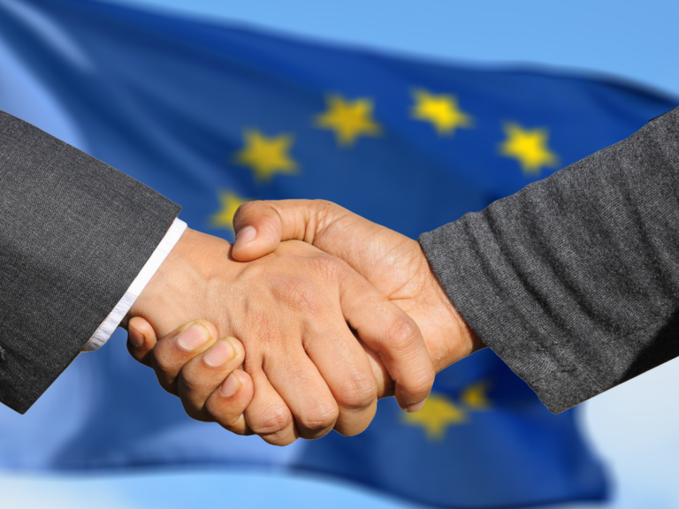 Two people shaking hands in front of a blue European Union flag